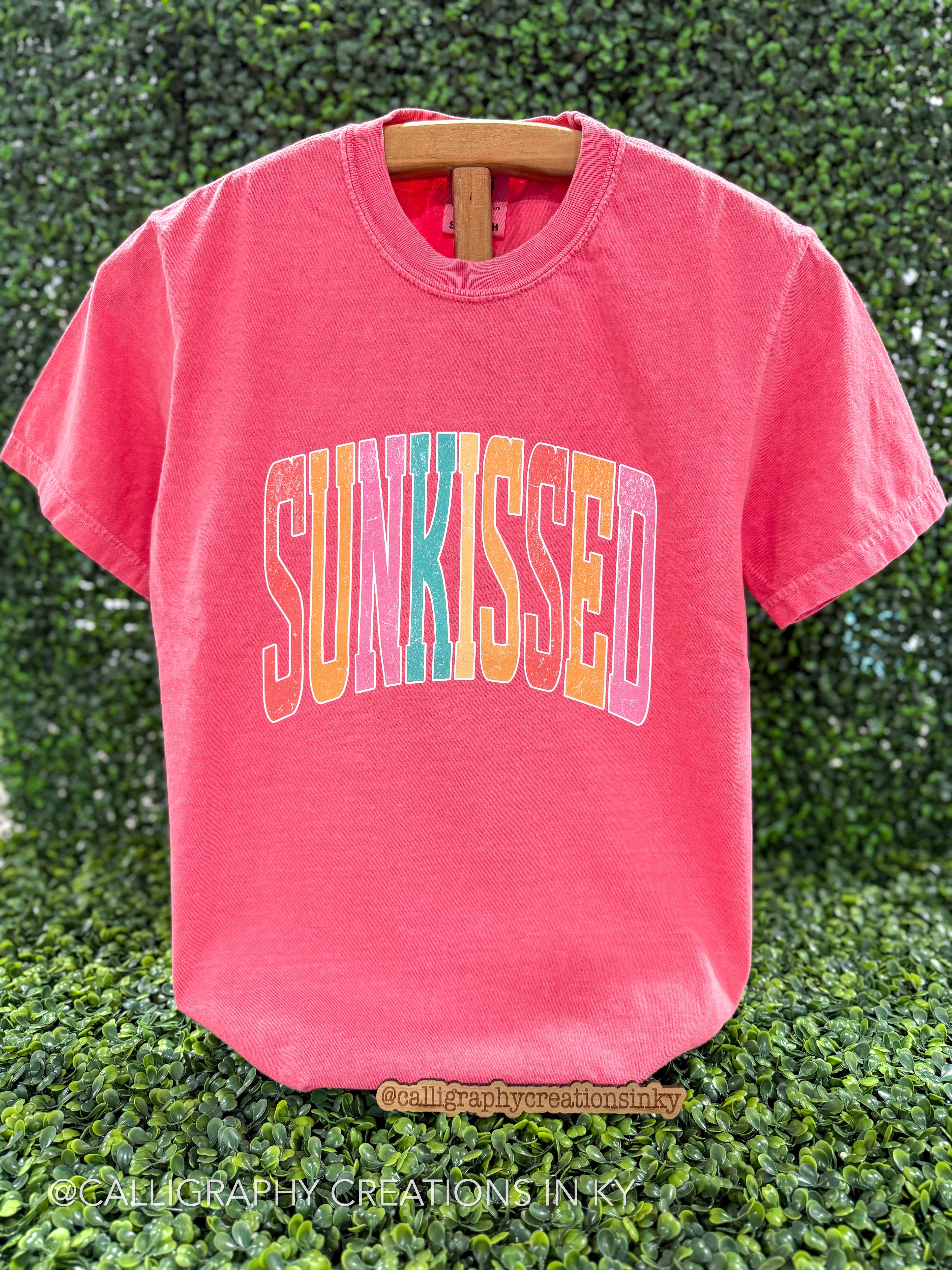 Watermelon colored tshirt with a colorful text design that says “Sun-kissed”