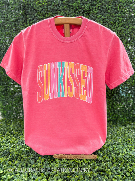Watermelon colored tshirt with a colorful text design that says “Sun-kissed”