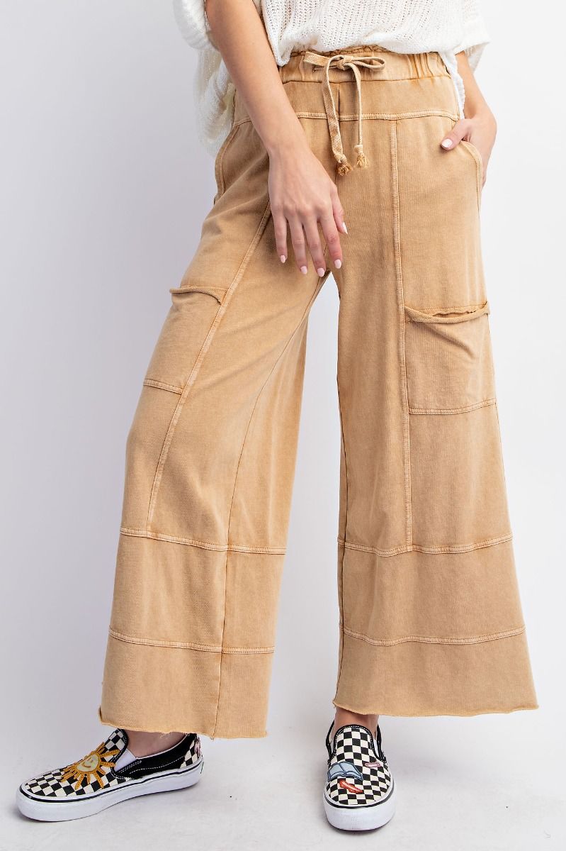 A person standing wearing beige mineral washed terry knit pants with cargo style pockets and an elastic ruched waist with an adjustable drawstring.
