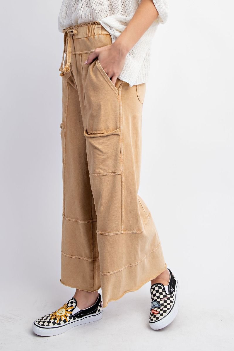 The side of a person standing wearing beige mineral washed terry knit pants with cargo style pockets and an elastic ruched waist with an adjustable drawstring.