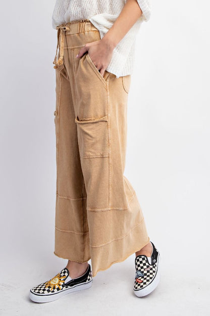 The side of a person standing wearing beige mineral washed terry knit pants with cargo style pockets and an elastic ruched waist with an adjustable drawstring.