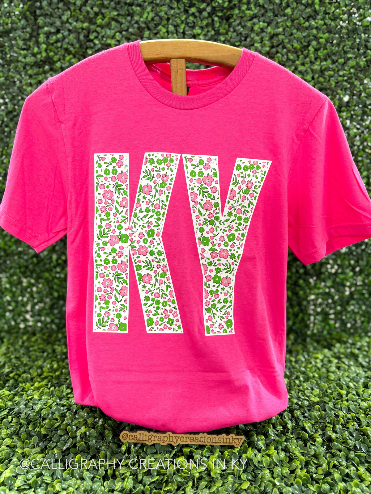 Pink shirt with floral ‘KY’ on a wooden stand 