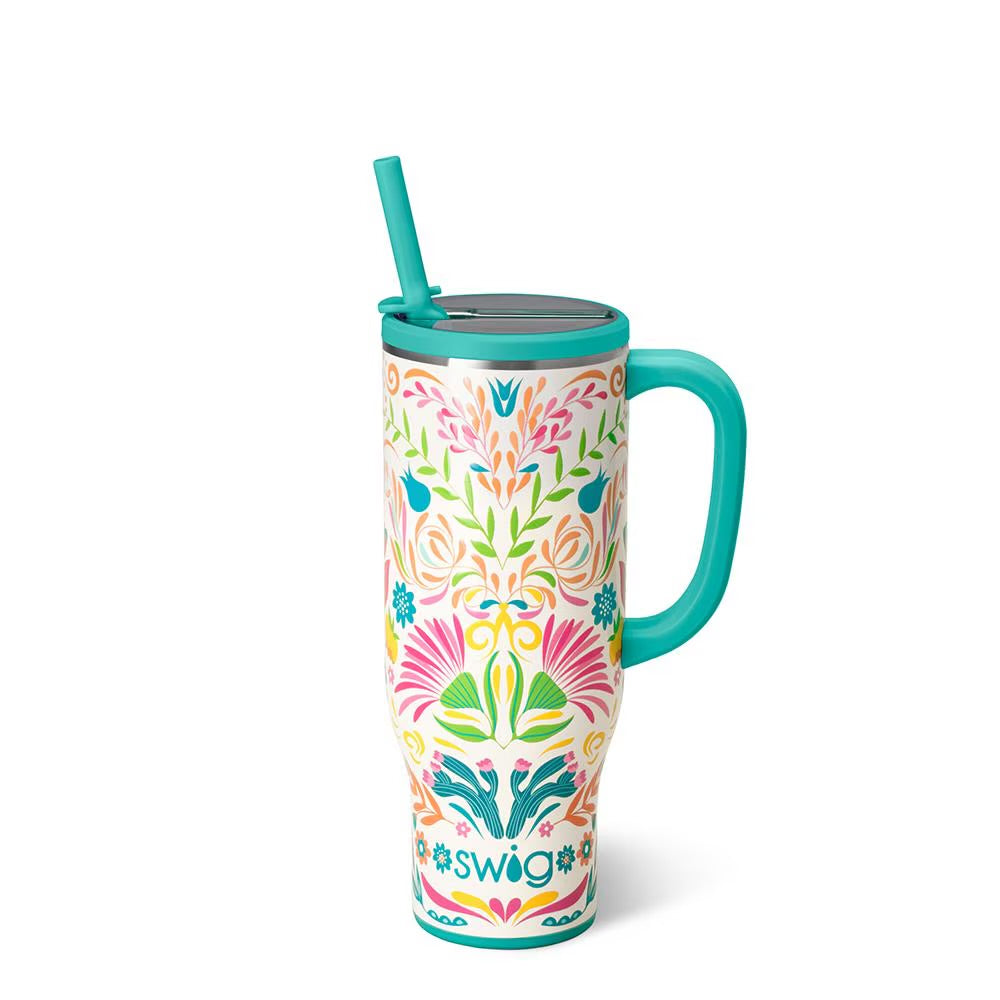 A tall handled travel tumbler with a colorful floral pattern on a white background, featuring a turquoise handle, lid, and straw, and the SWIG logo at the bottom.