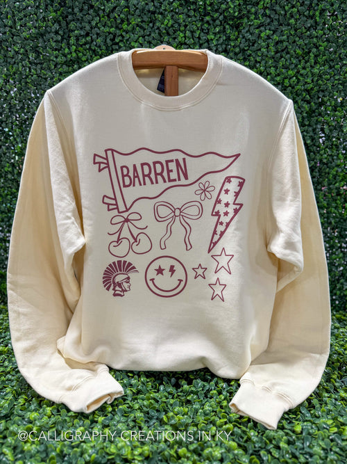 A cream-colored crewneck sweatshirt with a maroon graphic print featuring the word 'BARREN' on a pennant flag, along with bicycle, bow, lightning bolt, stars, and a smiley face, displayed on a wooden hanger against a green leaf wall.