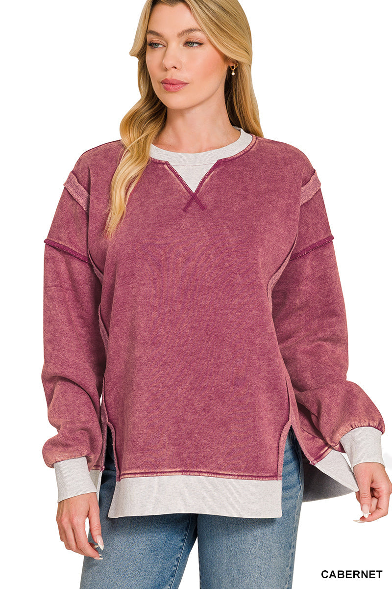 A woman wearing a cabernet mauve acid-wash long-sleeve sweatshirt with contrast ribbed trim over a white crewneck undershirt and blue jeans, on a white background.