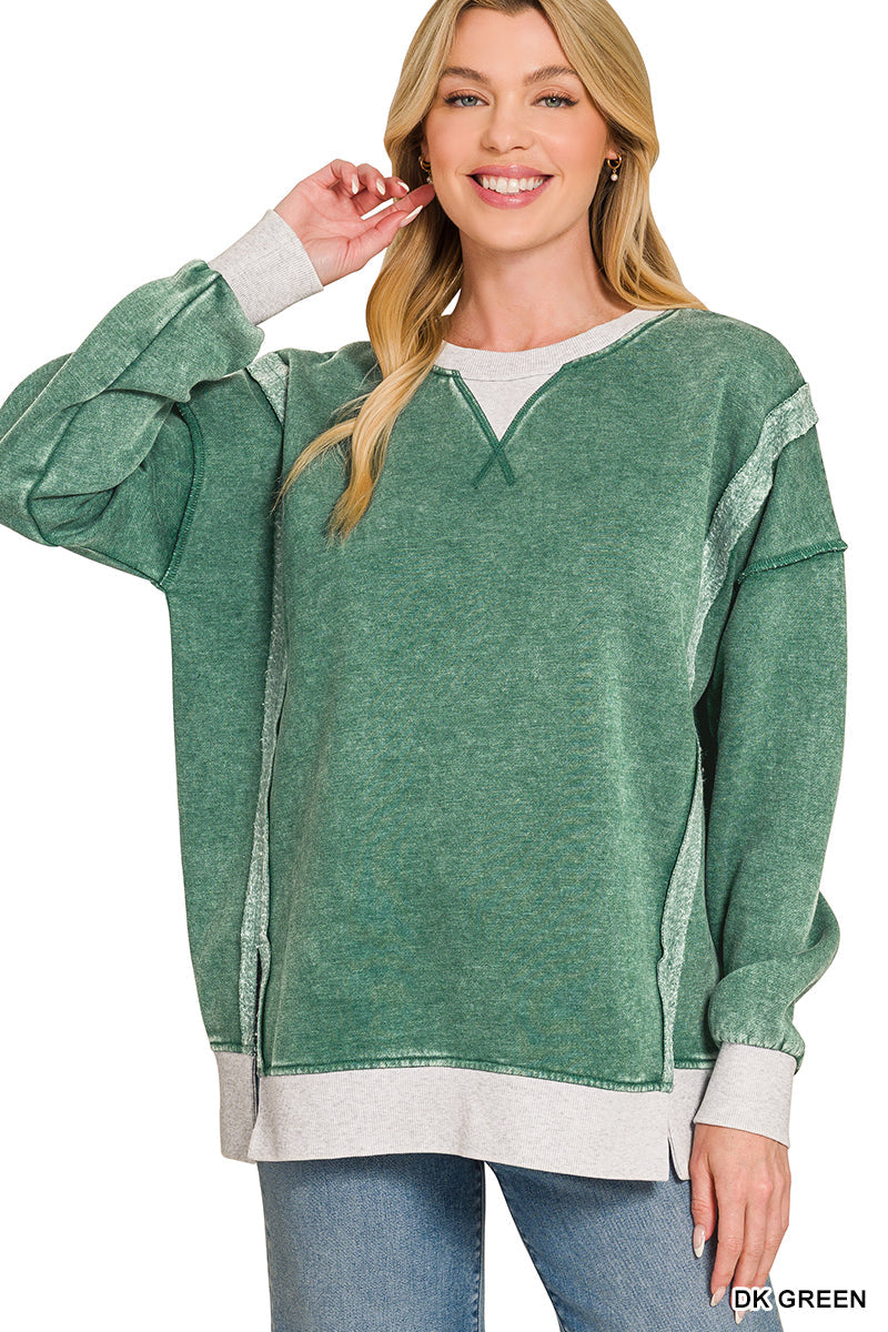 A woman modeling a green heathered long-sleeve sweatshirt with contrasting light gray ribbed trim at the crew neck, cuffs, and hem, paired with blue jeans against a white background.