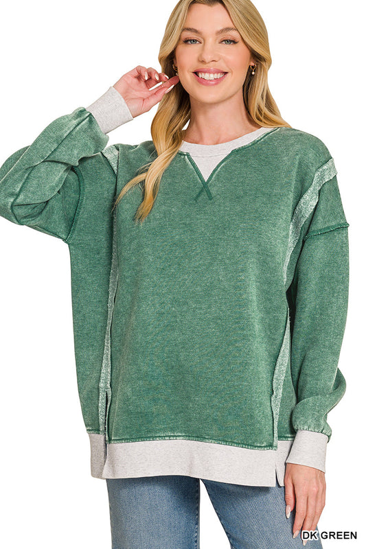 A woman modeling a green heathered long-sleeve sweatshirt with contrasting light gray ribbed trim at the crew neck, cuffs, and hem, paired with blue jeans against a white background.