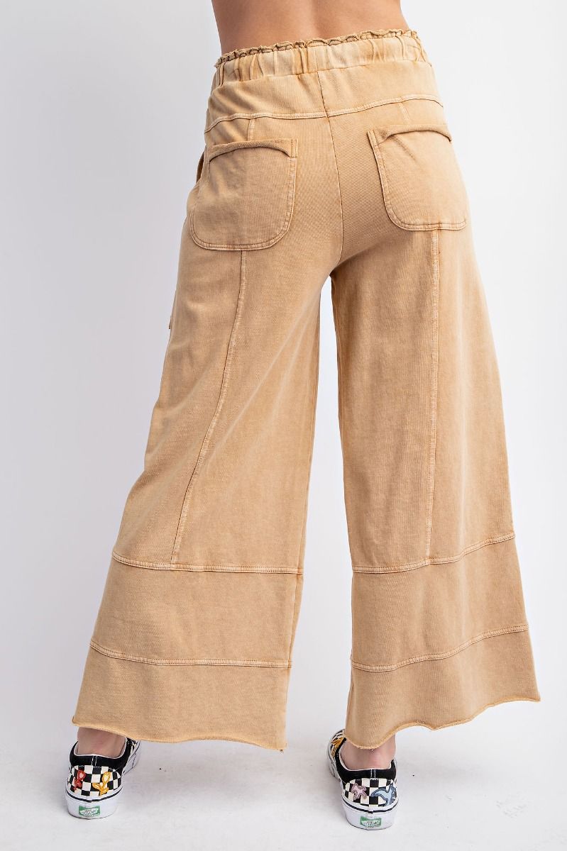 The back of a person standing wearing beige mineral washed terry knit pants with cargo style pockets and an elastic ruched waist with an adjustable drawstring.