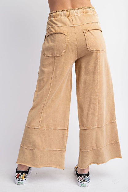 The back of a person standing wearing beige mineral washed terry knit pants with cargo style pockets and an elastic ruched waist with an adjustable drawstring.