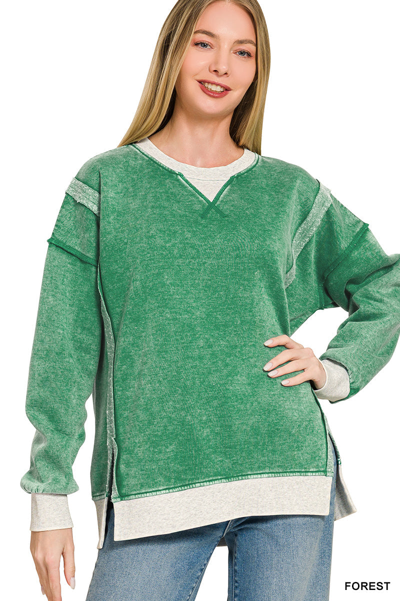A woman wearing a forest green long-sleeve sweatshirt with heather gray ribbed trim and side slits, paired with blue jeans, against a plain white background.