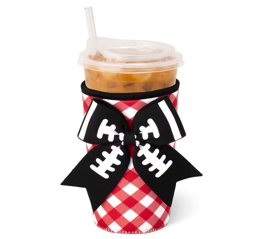 A red and white gingham-patterned cup sleeve with a large black ribbon bow featuring white football line details, shown on a clear-lidded iced coffee cup against a white background.