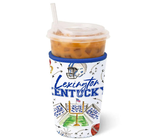 A clear plastic insulated tumbler with a clear lid and straw, filled with an iced orange-brown drink, wrapped in a white Lexington Kentucky football-themed sleeve with blue lettering and illustrated stadium graphics.