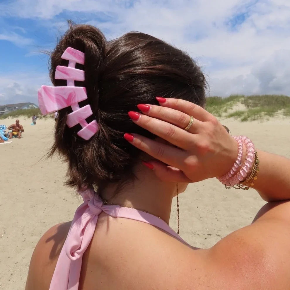 Person on a beach with pink hair clip and bracelet, wearing a pink top.