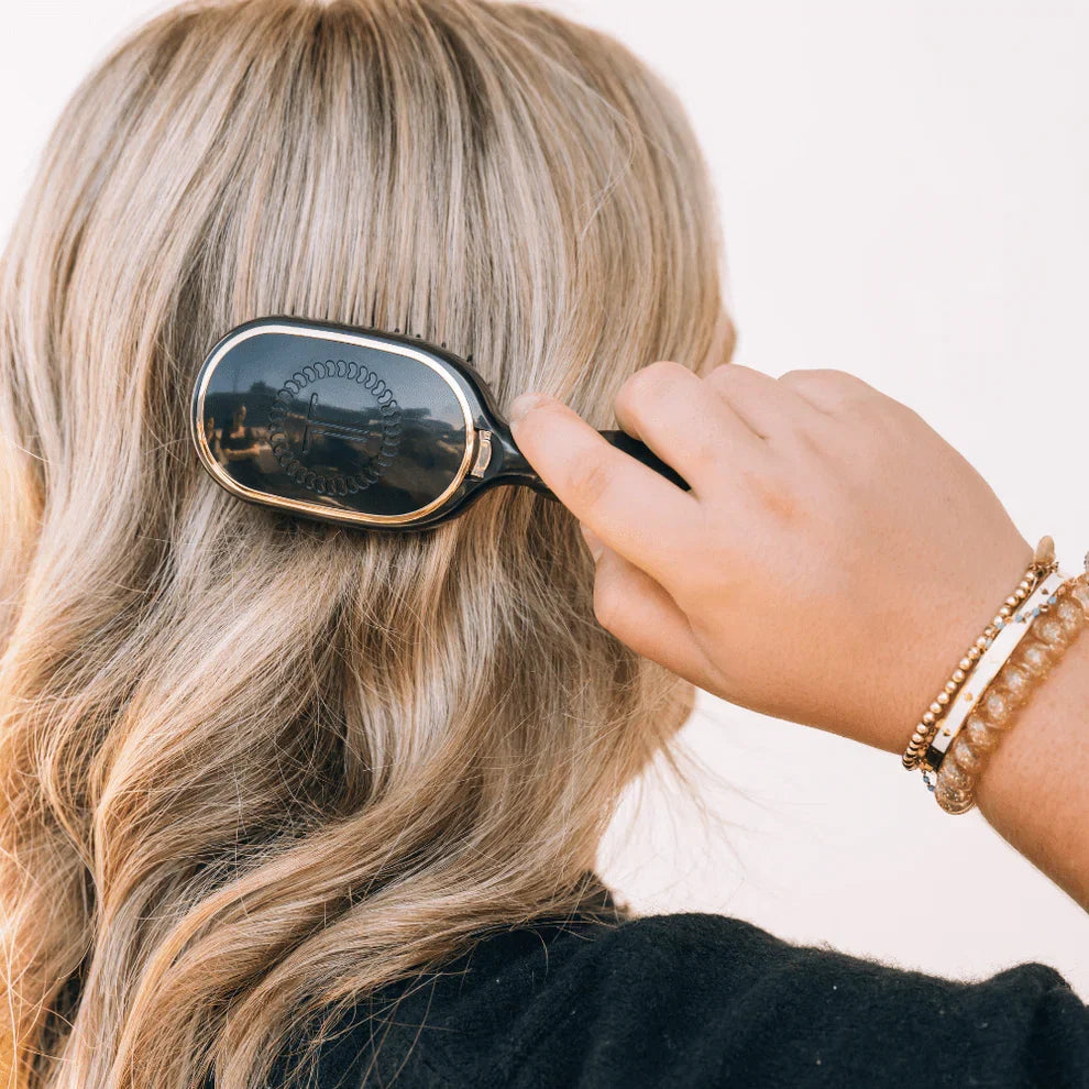 Person brushing their blonde hair with a black hairbrush on a light background