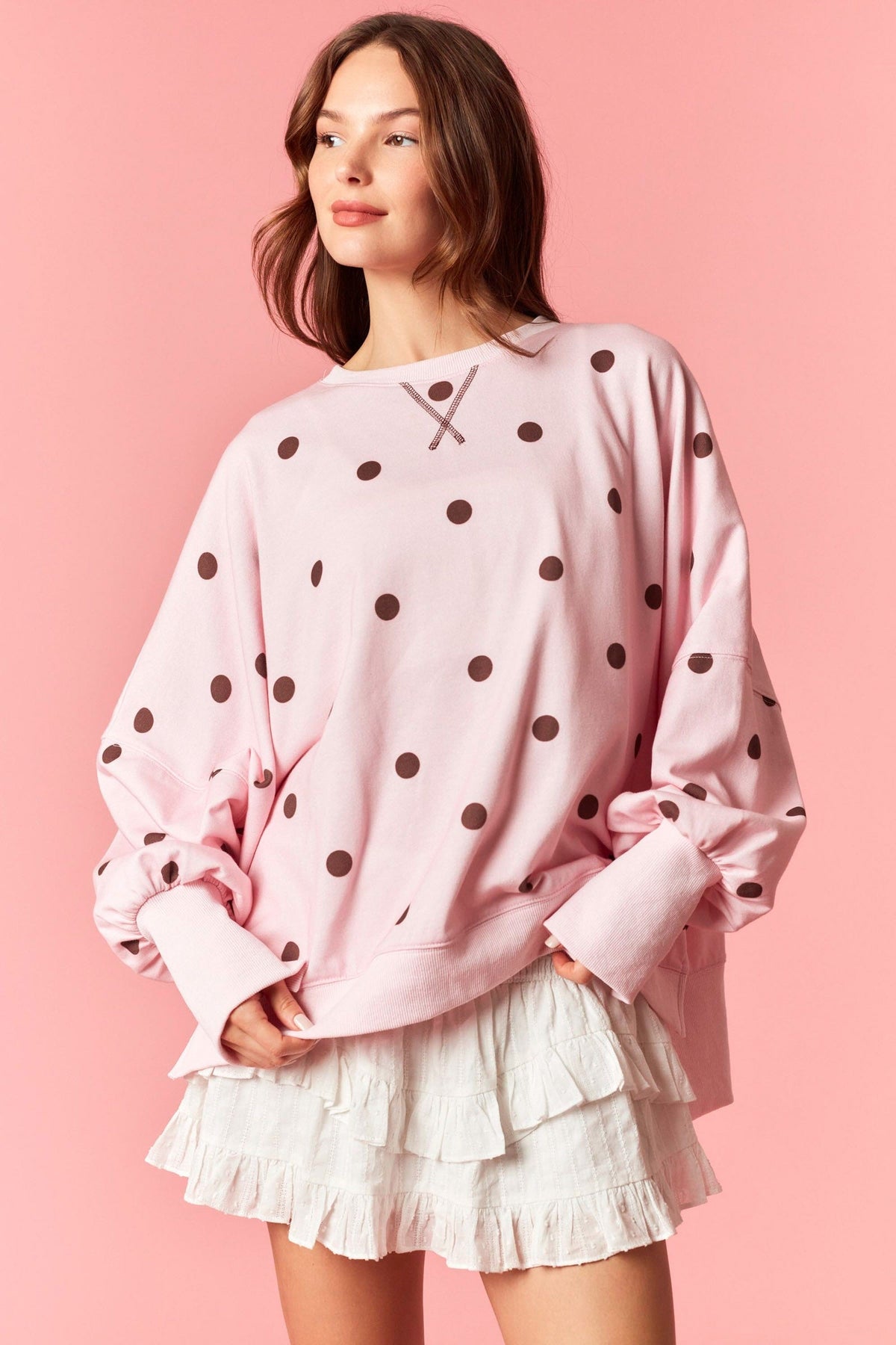 Woman wearing a pink polka dot sweater and white skirt against a pink background
