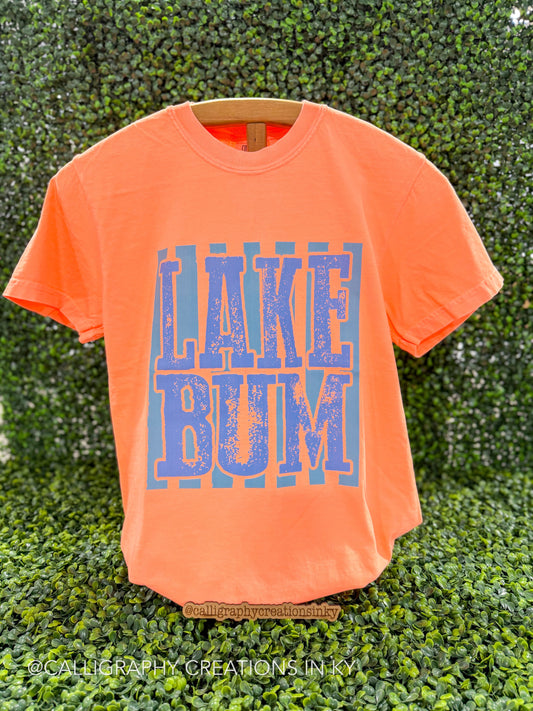 Bright coral shirt with teal striped and blue ‘Lake bum’ on a wooden stand 