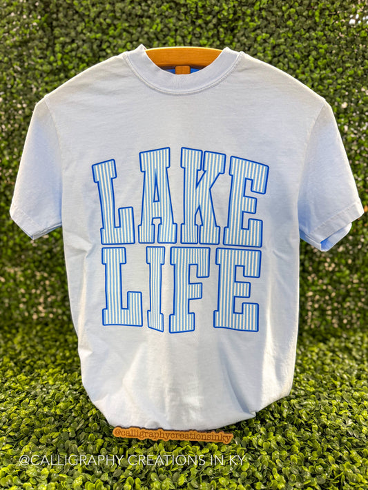Blue shirt with blue and white striped letters spelling ‘Lake Life’ on a wooden stand 
