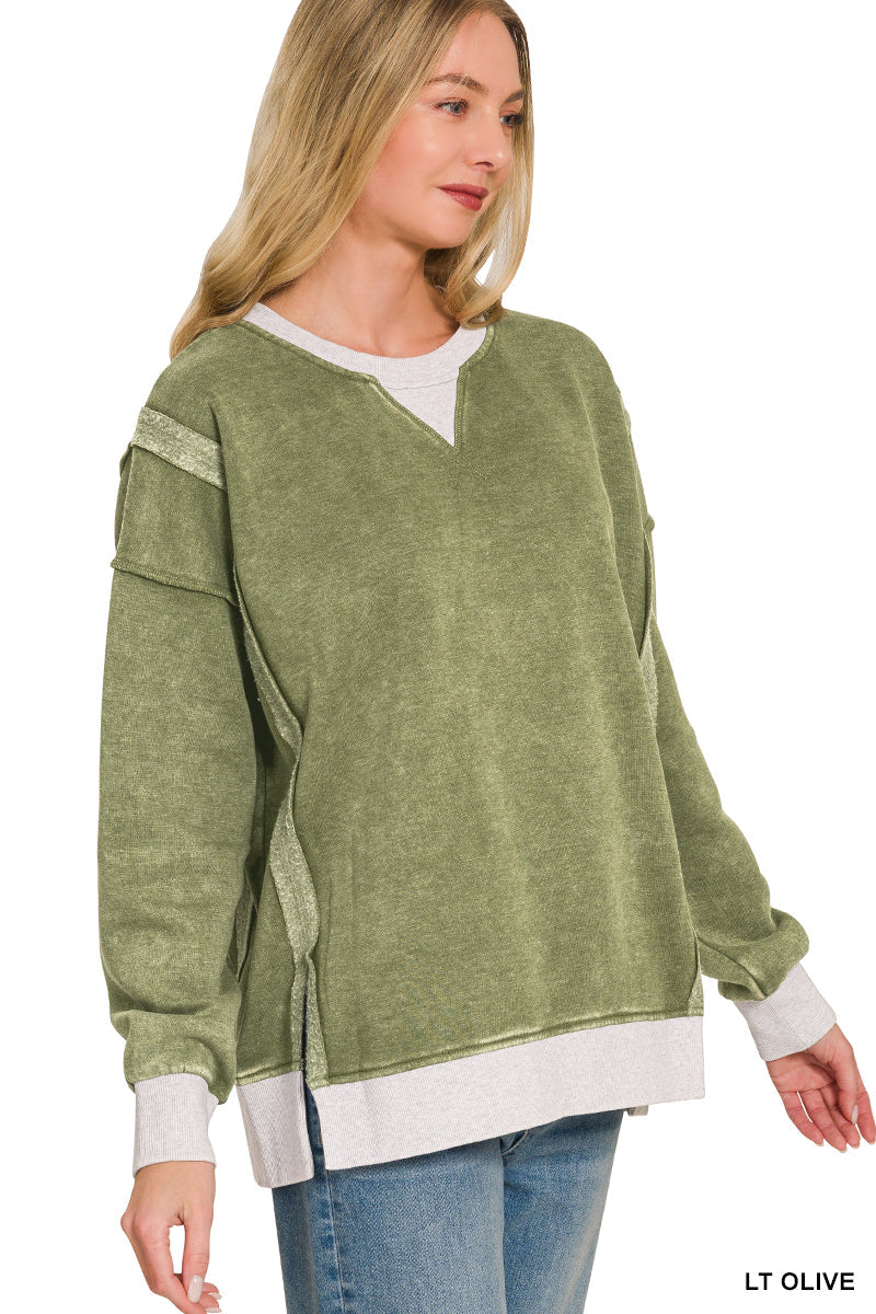 Woman wearing a light olive green sweater with white trim on a plain background