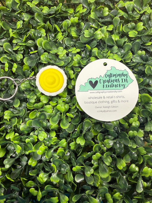 Keychain with yellow center and white border on green leafy background
