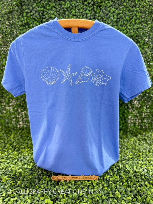 Blue shirt with white shells printed across the chest on a wooden stand 