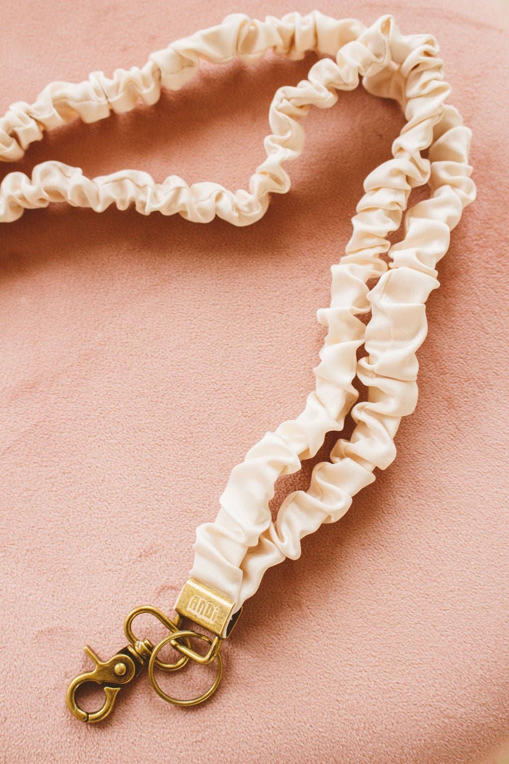 Cream scrunchie lanyard with gold clasp on a pink velvet background 