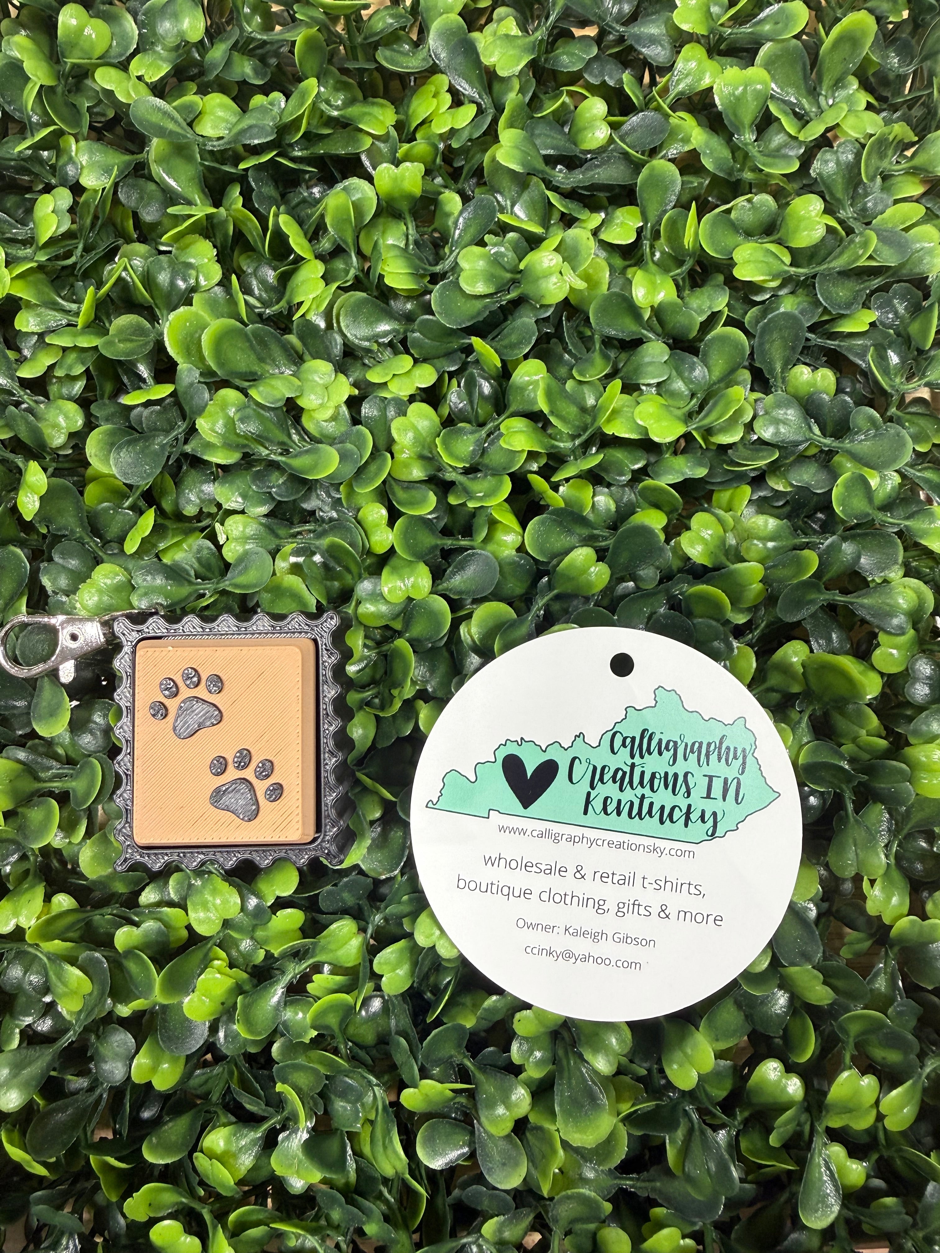 Paw print stamp keychain on a green leafy background