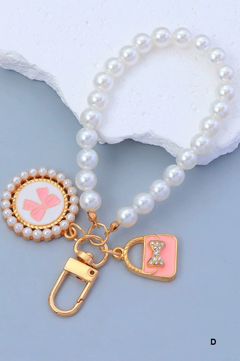 Pearl keychain with pink and gold bow and purse charms with gold clasps on a blue background 