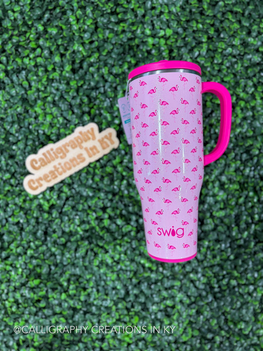 Pink tumbler with flamingo design on a green textured surface, featuring the brand 'Swig'.