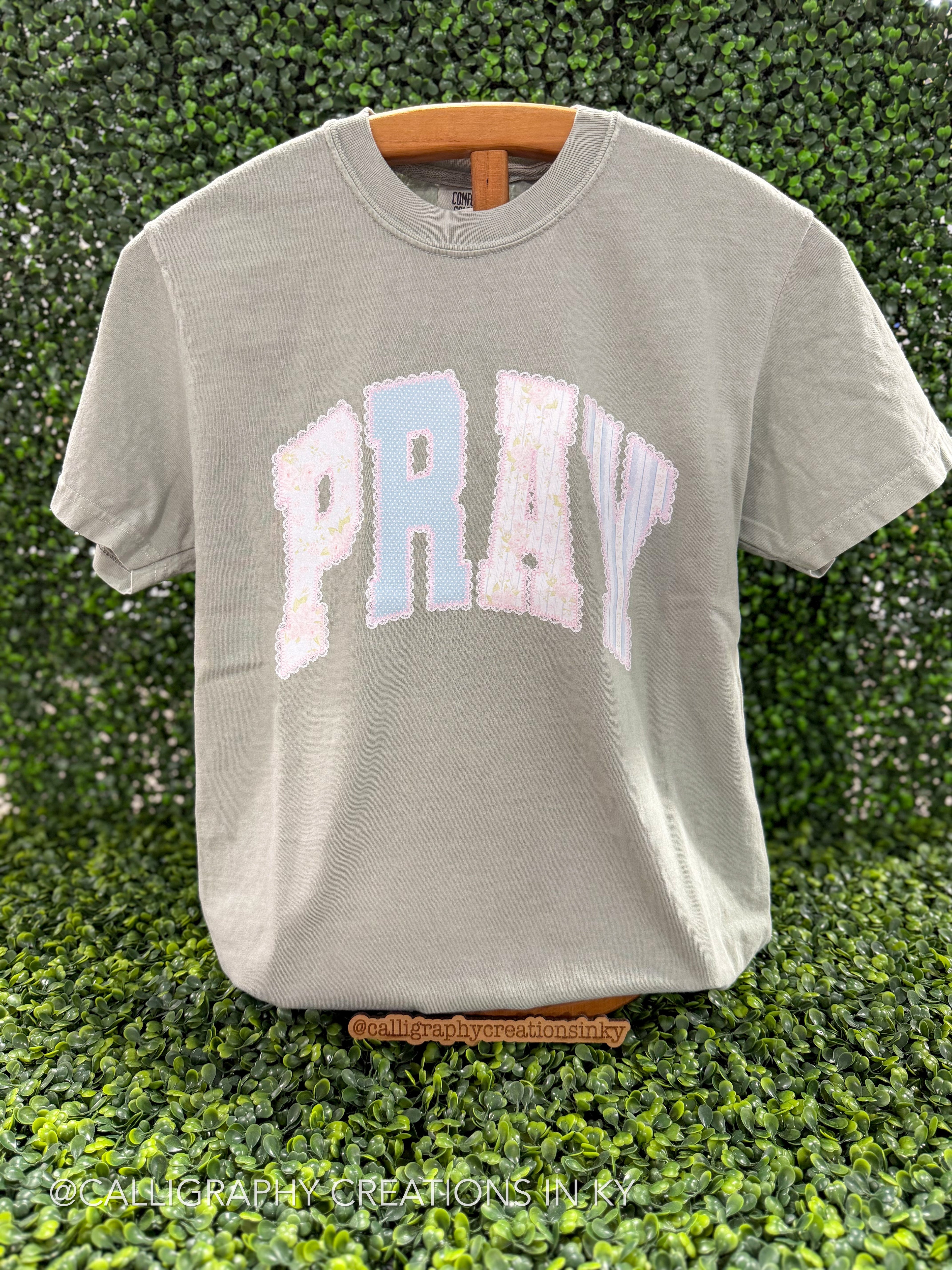 sage green shirt with pray with lace printed details on a wooden stand 