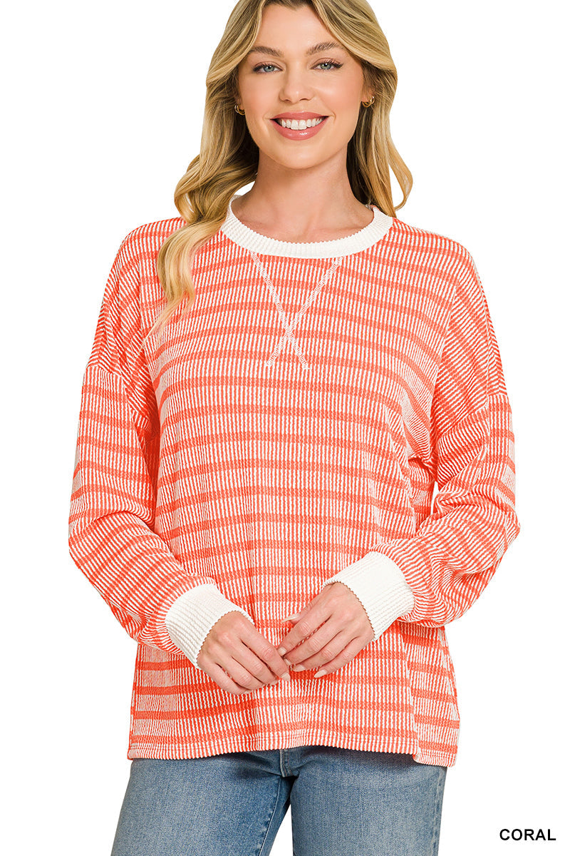 A woman wearing a coral and white horizontally striped long-sleeve knit top with white ribbed cuffs and collar, paired with blue jeans, against a plain white background.