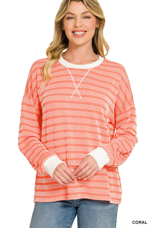 A woman wearing a coral and white horizontally striped long-sleeve knit top with white ribbed cuffs and collar, paired with blue jeans, against a plain white background.