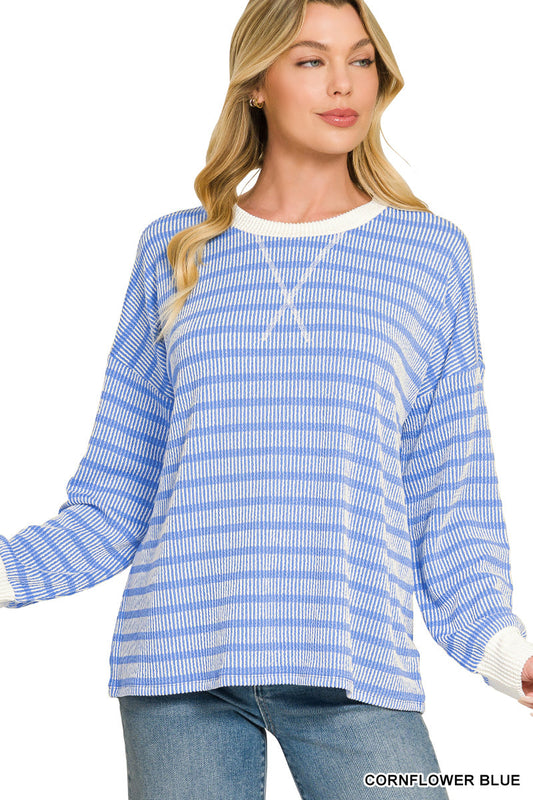 A woman wearing a long-sleeve knit top with horizontal cornflower blue and white stripes, paired with blue jeans, against a plain white background.