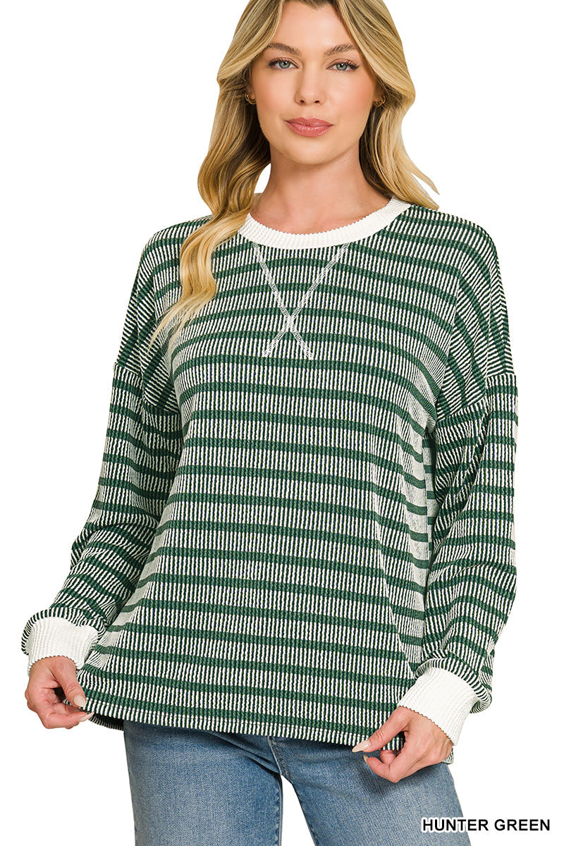 A woman modeling a long-sleeve knit top with horizontal green and white stripes, featuring a white crew neck and white ribbed cuffs, paired with blue jeans against a plain white background.