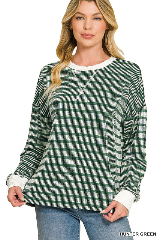 A woman modeling a long-sleeve knit top with horizontal green and white stripes, featuring a white crew neck and white ribbed cuffs, paired with blue jeans against a plain white background.