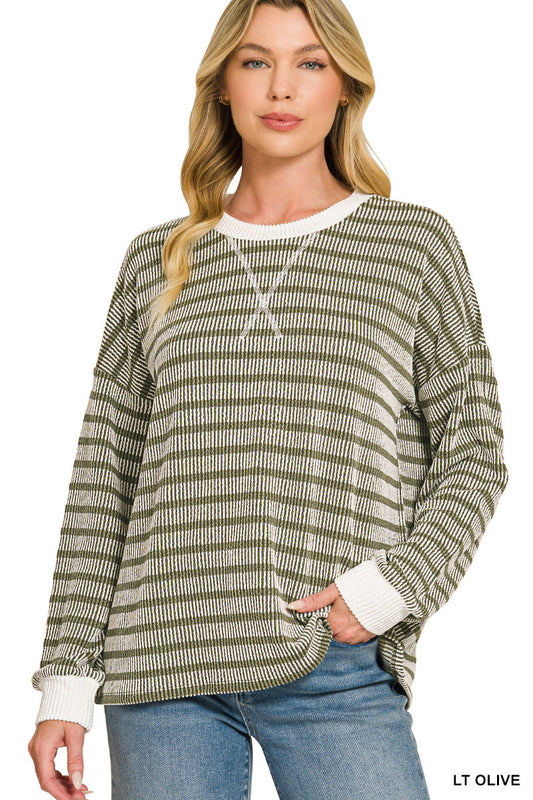 A woman modeling a long-sleeve knit sweater with horizontal olive green and cream stripes, featuring a cream crew neck and cuffs, paired with blue jeans against a white background.