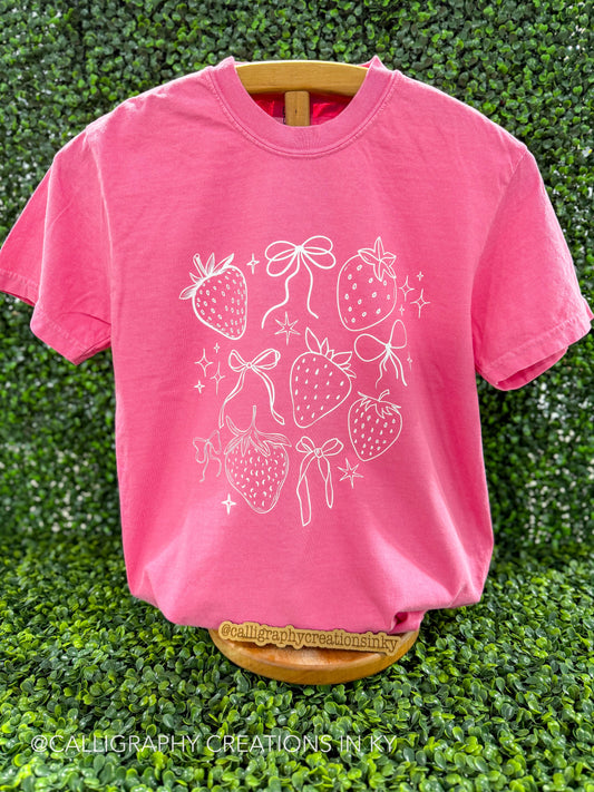 Pink shirt with strawberries and bows printed in white on a wooden stand