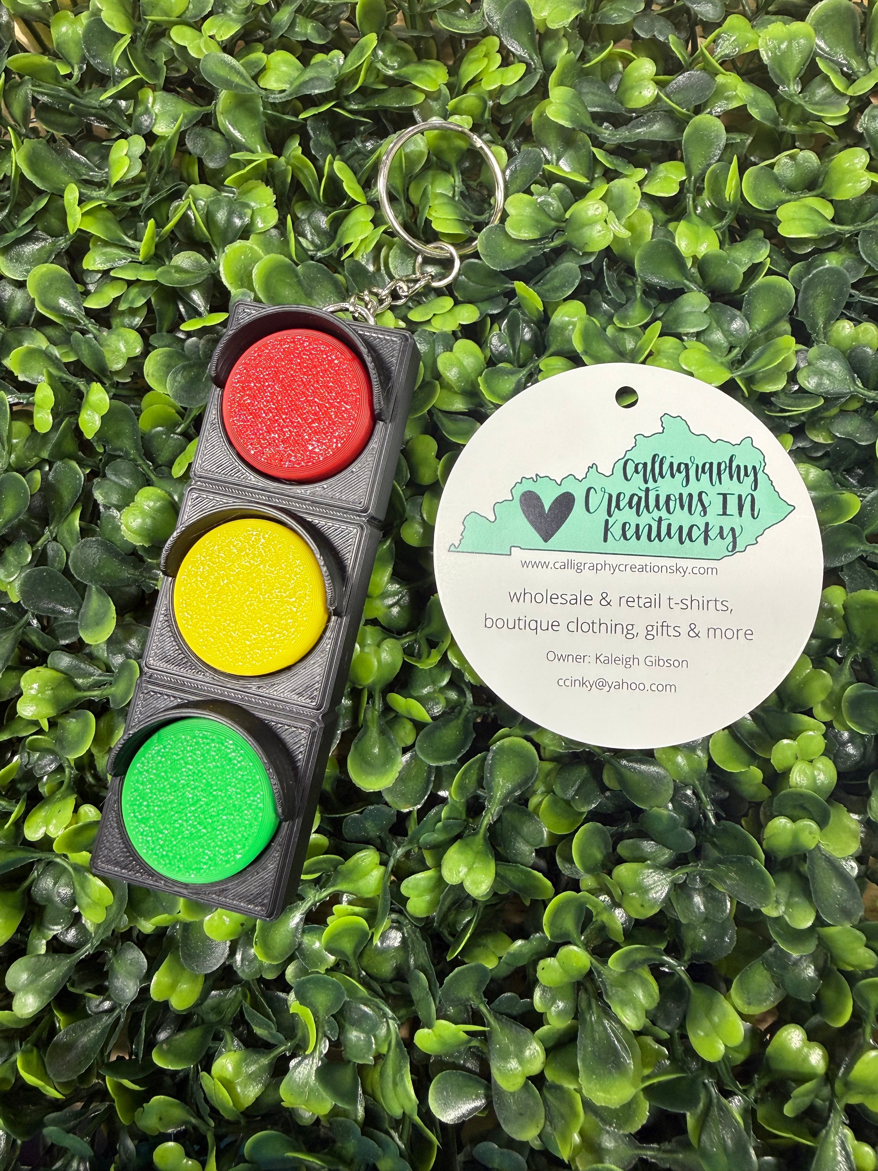 Keychain traffic light with red, yellow, and green buttons on a green leafy background