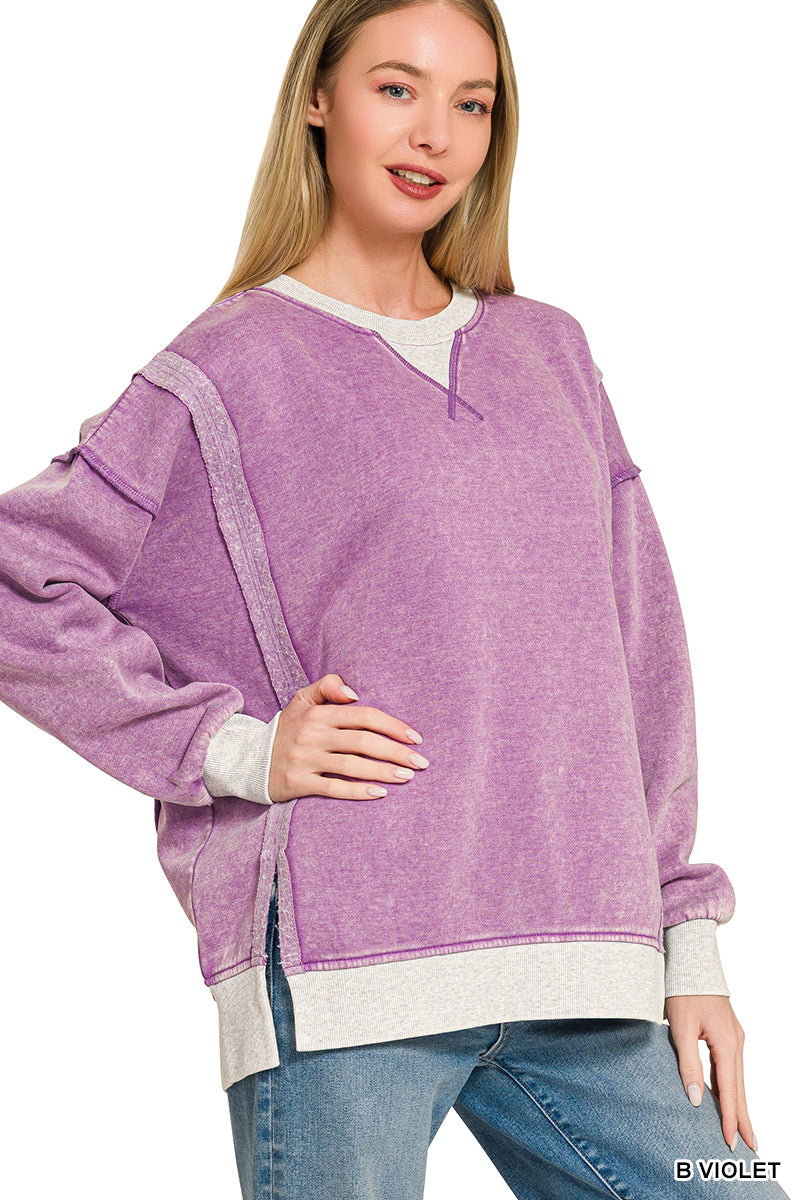 A woman modeling a lavender-purple knit sweater with contrast light gray ribbed trim at the split neckline, cuffs, and hem, paired with blue jeans against a plain white background.