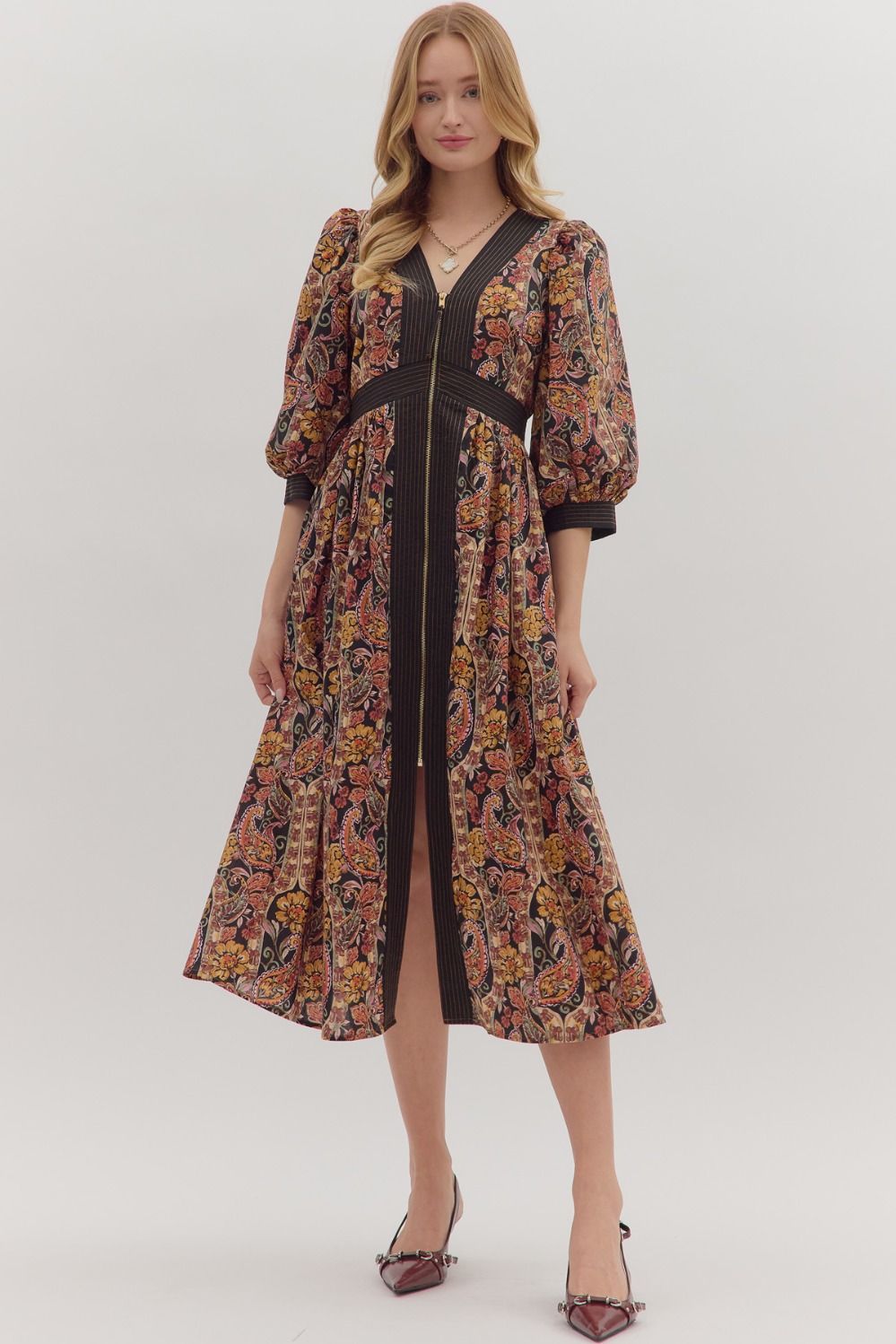 A paisley print midi dress with puff sleeves, striped trim, and a partial front zipper closure. The lightweight, woven fabric drapes beautifully, showcasing the dress’s flattering silhouette