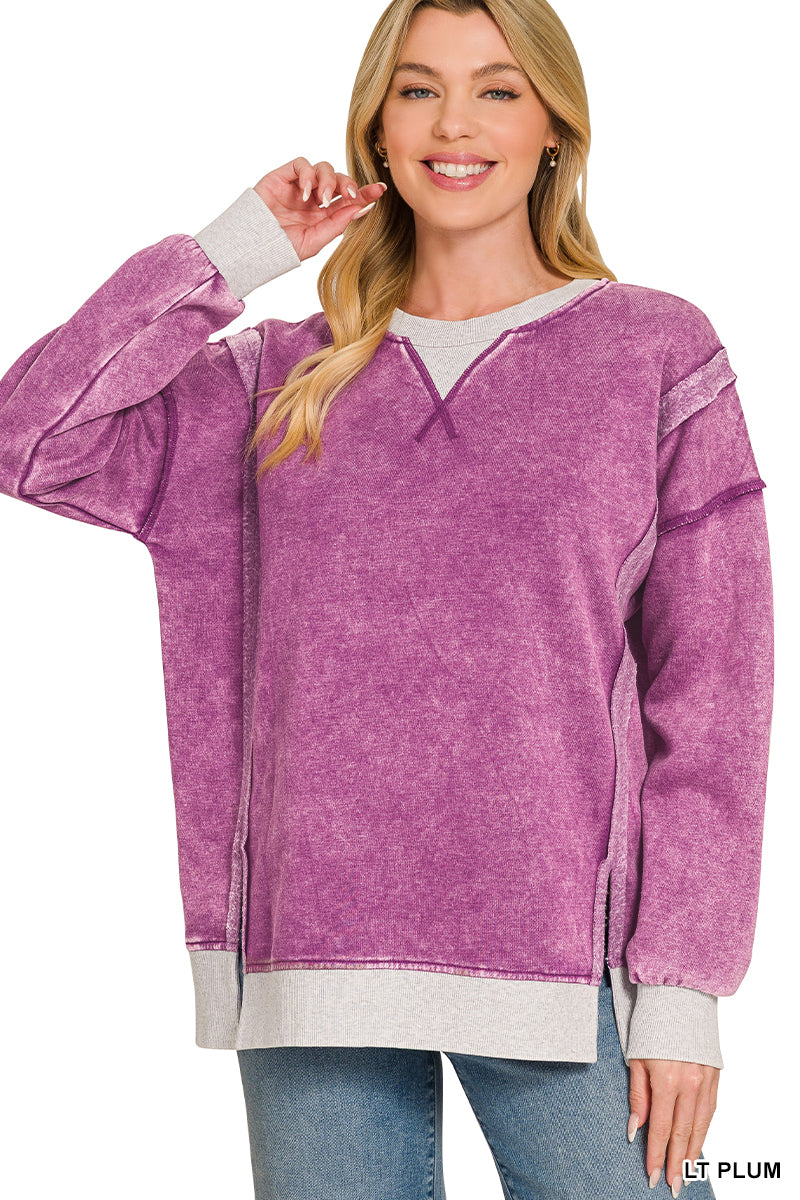 A woman wearing a purple acid-wash long-sleeve sweatshirt with contrasting light gray ribbed trim on the crew neck, cuffs, and hem, paired with blue jeans against a white background.