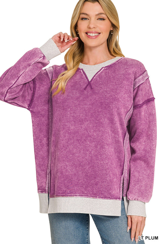 A woman wearing a purple acid-wash long-sleeve sweatshirt with contrasting light gray ribbed trim on the crew neck, cuffs, and hem, paired with blue jeans against a white background.